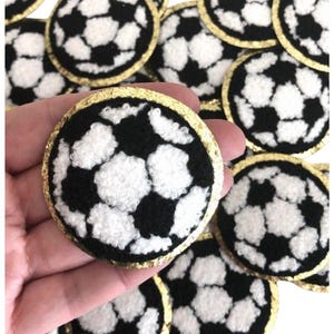 May include: A set of 12 black and white felt soccer ball patches with a gold glitter trim. The patches are approximately 2 inches in diameter.