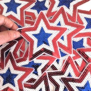 May include: A pile of red, white, and blue star-shaped sequins. The stars are layered on top of each other, creating a festive and patriotic look.