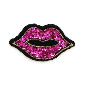 May include: Pink glitter lips with a black outline. The lips are made of sequins and have a gold trim.
