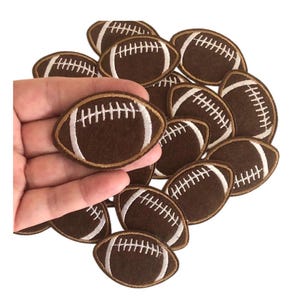 May include: A pile of brown felt football patches with white stitching. The patches are approximately 2 inches in diameter.