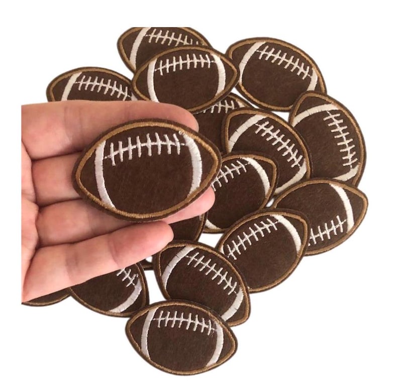 May include: A pile of brown felt football patches with white stitching. The patches are approximately 2 inches in diameter.