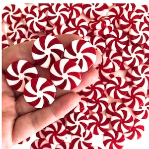 May include: A close-up of a hand holding a pile of red and white peppermint candies. The candies are round and have a swirl design.