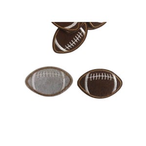 May include: Two felt footballs, one brown and one gray, with white stitching. The footballs are approximately 2 inches long.
