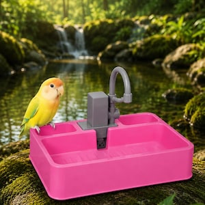 Puede incluir: Un bebedero rosa brillante con un grifo gris, sobre un fondo natural. Un pájaro amarillo y verde se posa en el borde. El bebedero tiene múltiples compartimentos para agua y comida.
