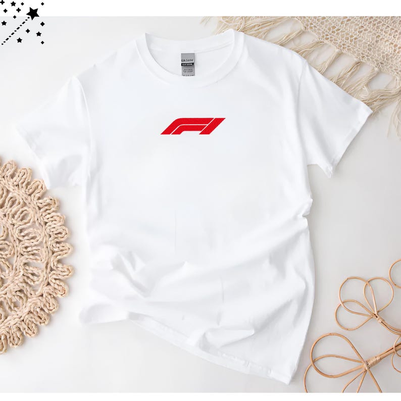 Op de afbeelding: Wit T-shirt met ronde hals en een rood F1-logo op de voorkant. Het logo is een gestileerd ontwerp met een rode balk en een schuine rode lijn. Het shirt is gemaakt van zacht, licht materiaal.