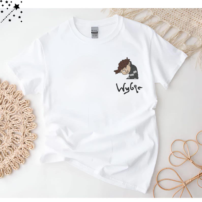 May include: White t-shirt with a cartoon illustration of a person with brown hair and a black and white outfit. The text "Wybie" is written below the illustration.