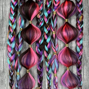 May include: Braided hair extensions in shades of black, teal, pink, and purple. The braids are adorned with decorative, bulbous accents in matching colors, accented with gold-colored metal. The overall effect is a vibrant and eye-catching hairstyle.