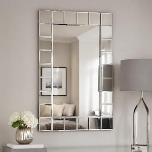May include: A rectangular wall mirror featuring a central reflective glass panel surrounded by a border of smaller, individual square mirrored tiles. The frame consists of these bevelled glass squares arranged in a grid pattern around the perimeter.