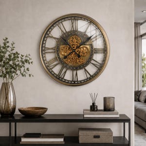 May include: A large round wall clock with a metallic gold frame and a transparent face. The centre features exposed gold-toned gears and the text KENSINGTON. It has black Roman numerals and black clock hands, displaying a mechanical design.