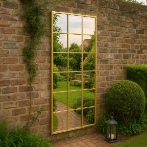 May include: A rectangular wall mirror featuring a gold-coloured metal frame divided into a grid of fifteen individual glass panes. The mirror reflects a garden scene with a wooden bench, green trees, and a brick pathway, creating a window-like effect.