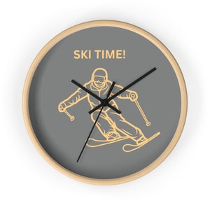 May include: A grey round clock with a wooden frame. The clock face features a yellow silhouette of a skier with the text "SKI TIME!" in yellow.
