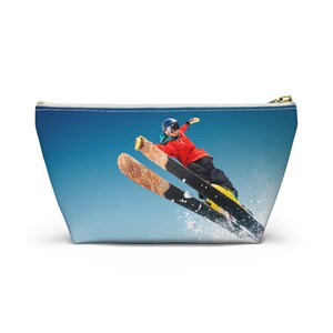 May include: A blue and white zippered pouch with a colorful image of a person skiing down a snowy slope.