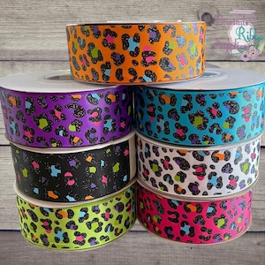 May include: A selection of leopard print ribbon rolls in various colours. The ribbons display a range of hues, such as orange, purple, teal, black, white, pink, and neon green. Each roll has a distinctive leopard spot design with black outlines and glitter detailing.