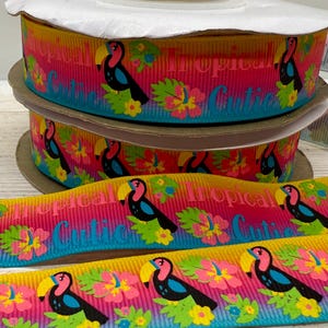 Könnte beinhalten: Rollen mit dekorativem Band mit tropischem Thema. Das Band zeigt einen Tukan, Hibiskusblüten und die Worte "Tropical Cutie" in einem farbenfrohen Farbverlauf. Das Band befindet sich auf einer Papprolle.