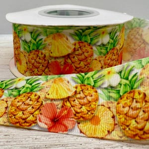 Könnte beinhalten: Eine Rolle dekoratives Band mit einem tropischen Ananas-Design. Das Band zeigt gelbe, orangefarbene und grüne Ananas, Hibiskusblüten und Blätter. Das Band eignet sich ideal zum Basteln und Geschenkverpacken.
