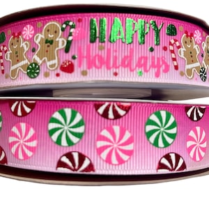 Könnte beinhalten: Zwei Rollen rosa Band mit festlichem Weihnachtsdesign. Die obere Rolle zeigt Lebkuchenmänner, Zuckerstangen und die Worte "Happy Holidays" in grünem Glitzer. Die untere Rolle hat ein Muster aus Pfefferminzbonbons.