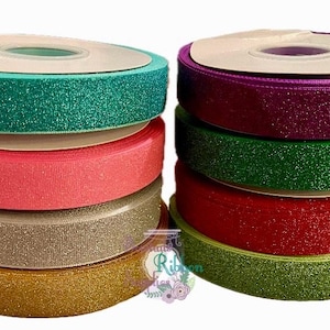 Può includere: Un set di 10 bobine di nastro glitterato in vari colori, tra cui verde, viola, rosa, argento, oro e rosso. Il nastro è avvolto attorno a bobine di cartone.