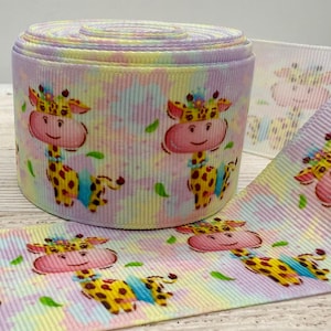 Può includere: Un rotolo di nastro dai colori pastello con un motivo ripetuto di una giraffa dei cartoni animati. La giraffa ha una faccia rosa, macchie gialle e un colletto blu. Accenti di foglie verdi sono sparsi intorno alle giraffe. Una lunghezza di nastro è srotolata.