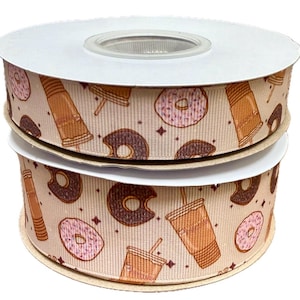 Puede incluir: Dos carretes de cinta beige con un patrón repetido de donuts, tazas de café y estrellas. Los donuts son rosados con chispas blancas y marrones con glaseado blanco. Las tazas de café son marrones con una pajita.