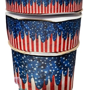 Op de afbeelding: Drie rollen patriottisch lint. Het lint heeft een ontwerp van blauw met witte sterren en rood-witte strepen. Het lint is geschikt voor knutselen en decoreren voor patriottische feestdagen.