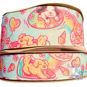 May include: Two rolls of light blue and pink ribbon with a white background. The ribbon features a repeating pattern of cartoon dogs, hearts, and rainbows. The ribbon is labelled "Bows & Ribbon Supplies".