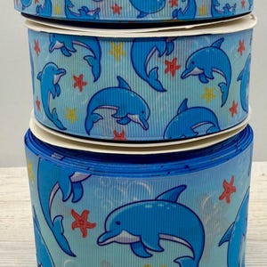 Könnte beinhalten: Drei Rollen blaues Band mit weißem Hintergrund und einem sich wiederholenden Muster aus blauen Delfinen, roten Seesternen und gelben Sternen.