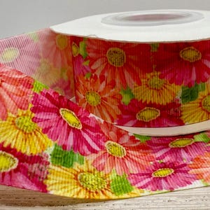 May include: A spool of pink and yellow floral ribbon with a white background. The ribbon features a watercolour-style print of pink and yellow flowers.
