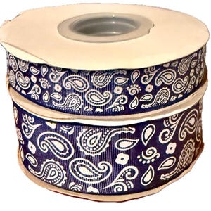 Könnte beinhalten: Zwei Rollen marineblaues Band mit weißem Paisley-Muster. Das Band ist übereinander gestapelt, mit einem weißen Pappkern und einer transparenten Kunststoffmitte.