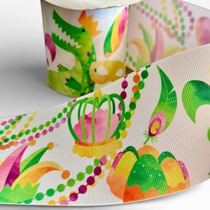 Könnte beinhalten: Weißes Band mit einem sich wiederholenden Muster von Mardi-Gras-Illustrationen. Das Design umfasst ein grünes Alligator, eine Krone, bunte Federn und Perlenketten. Das Band ist aufgerollt, mit einem abgerollten Teil, der das vollständige Muster zeigt.