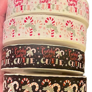 May include: Four rolls of Christmas ribbon featuring a candy cane and "Candy Cane Cute" design. The ribbon is white with pink and red candy canes, black with pink and red candy canes, and black with silver glitter candy canes.