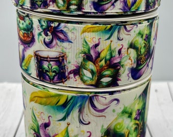 May include: Three spools of white satin ribbon with a Mardi Gras theme. The ribbon features a colorful watercolor design of masks, feathers, drums, and hats. The ribbon is perfect for crafting, decorating, and adding a festive touch to any project.