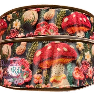 May include: A close-up of a red and white mushroom print ribbon with green foliage and pink flowers. The ribbon is on a brown spool.