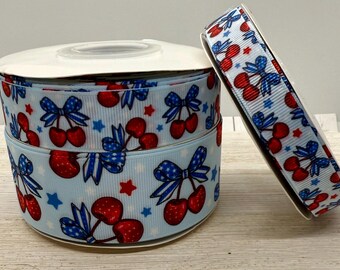 May include: A spool of blue and white ribbon with a red cherry and star pattern. The ribbon is wrapped around a white cardboard spool.