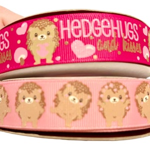 Könnte beinhalten: Zwei Rollen pinkfarbenes Band mit einem Igel-Druck. Die obere Rolle hat den Text "Hedgehugs and Kisses" in goldenen Buchstaben. Die untere Rolle hat ein sich wiederholendes Muster aus braunen Igeln mit rosa Herzen auf einem rosa Hintergrund.