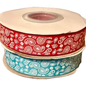 Könnte beinhalten: Zwei Rollen Band, eine rote und eine türkisfarbene, jeweils mit einem weißen Paisley-Muster. Das Band wird wahrscheinlich zum Basteln, zum Verpacken von Geschenken oder für andere dekorative Zwecke verwendet. Die Rollen sind übereinander gestapelt.
