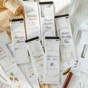 Könnte beinhalten: Dekorative Papierstreifen mit schwarzen Rändern, die Texte und Designs wie "Yesterday's Narrative" und "Flower Shadow" aufweisen. Die Streifen sind auf einer strukturierten Oberfläche angeordnet.