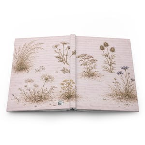 Pode incluir: Diário aberto com uma ilustração botânica. A capa e as páginas apresentam desenhos detalhados de várias flores silvestres e ervas em tons de bege, castanho e verde. O diário está aberto, exibindo a obra de arte detalhada em ambas as páginas.