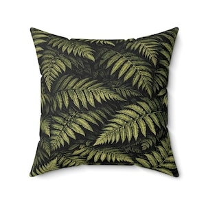 May include: Square cushion with a fern leaf design. The cushion has a dark background with a repeating pattern of green fern leaves. The cushion is square and appears to be made of a soft fabric.
