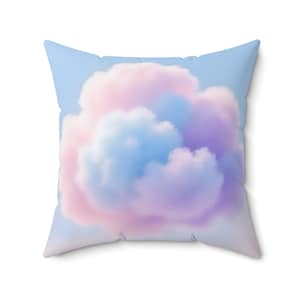 May include: Square throw pillow with a cloud design. The pillow features a light blue background with a fluffy cloud in shades of pink, purple, and blue. The pillow is square and appears to be made of a soft fabric.