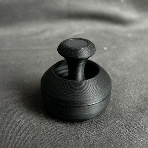 May include: A black rubber stamp with a round base and a circular top. The top has a raised, textured surface.