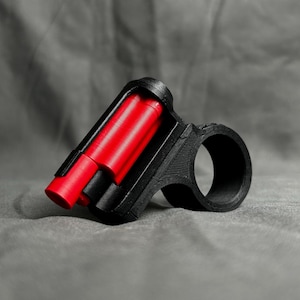May include: A black plastic bike mount with a red tube inside. The mount is designed to hold a small object, such as a phone or a flashlight.