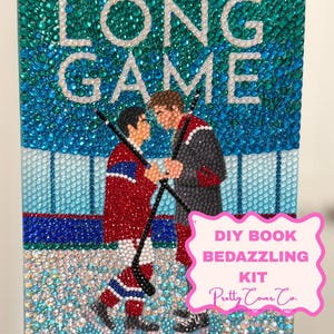 May include: A book cover titled The Long Game by Rachel Reid, decorated with colorful rhinestones. The image depicts two hockey players facing each other on ice. A pink scalloped label on the right reads DIY BOOK BEDAZZLING KIT Pretty Cover Co.