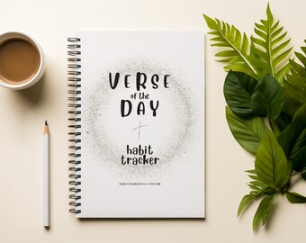 May include: A white spiral bound notebook with the text "VERSE of the DAY + habit tracker" on the cover. The notebook is on a white surface with a cup of coffee and a pencil.
