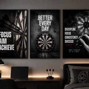 May include: A set of three framed wall art prints featuring dartboard imagery. The first print displays darts and the text FOCUS AIM ACHIEVE. The second shows a dartboard and the text BETTER EVERY DAY. The third shows a dart and the text DISCIPLINE FOCUS CONSISTENCY SUCCESS ONE THROW AT A TIME.