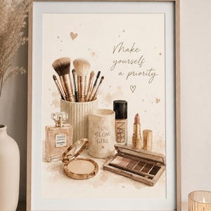 Puede incluir: Una lámina enmarcada estilo acuarela con brochas de maquillaje en un soporte estriado, un frasco de perfume Coco Chanel, un compacto, una base Nars, un pintalabios y un recipiente con el texto You Glow Girl y Make yourself a priority.