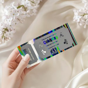 May include: A silver concert ticket with iridescent edges. The ticket says "Coldplay" with the date "February 23 202" and "Glasgow" printed on it. The ticket is held by a person.
