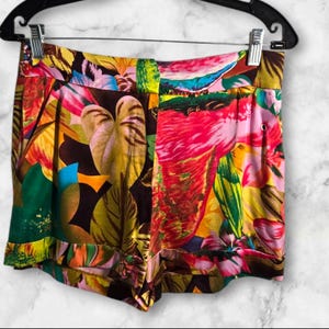 Puede incluir: Shorts de estampado tropical colorido con un flamenco rosa, hojas verdes y flores amarillas sobre un fondo marrón oscuro.