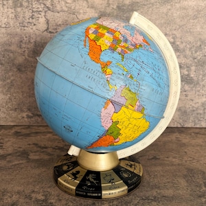 May include: A vintage globe with a blue ocean and colorful continents. The globe has a white meridian ring and sits on a base with zodiac symbols. The base is black and gold. The globe is a decorative item.