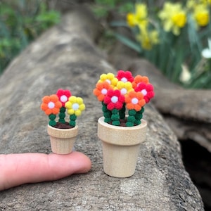 May include: Two miniature potted plants with colorful felt flowers. The larger plant has six flowers in shades of orange, yellow, and red. The smaller plant has three flowers in orange, yellow, and white. Both plants are in wooden pots.