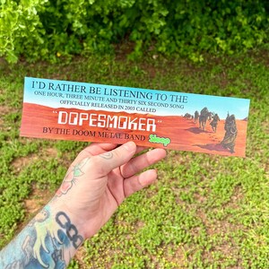 May include: A rectangular sticker with the text "I'D RATHER BE LISTENING TO THE" at the top. The sticker features the text "DOPESMOKER" and "BY THE DOOM METAL BAND Sleep". The background depicts a desert scene.